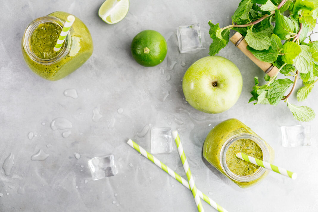 Green healty drink in mason jar with green apple, mint, lime and melting ice cubes on grey background. Vegetarian food concept. Detox