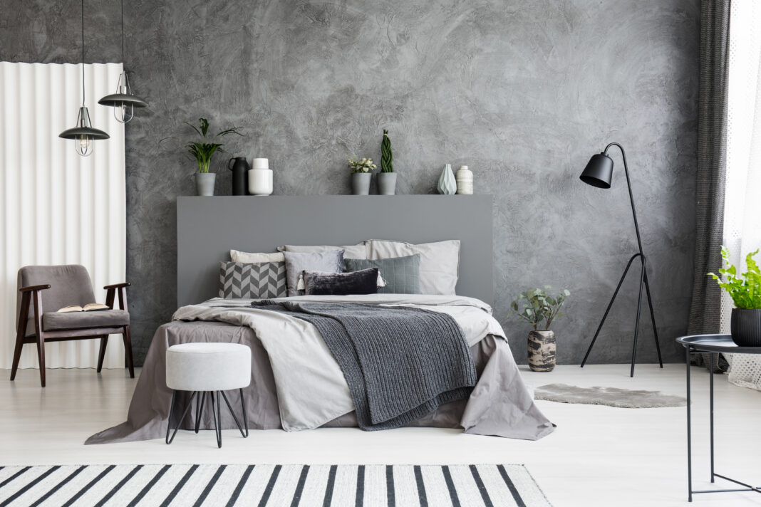 Grey armchair and stool near bed with headboard in bedroom inter