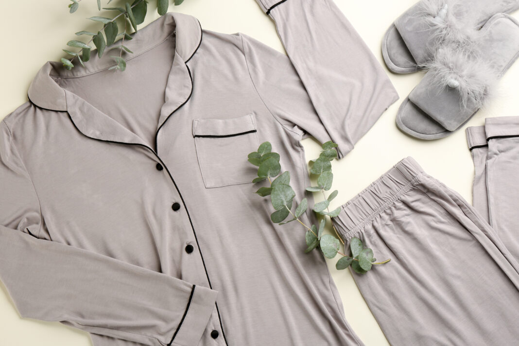 Pair of fluffy slippers, pajamas and eucalyptus branches on beige background, flat lay. Comfortable home outfit