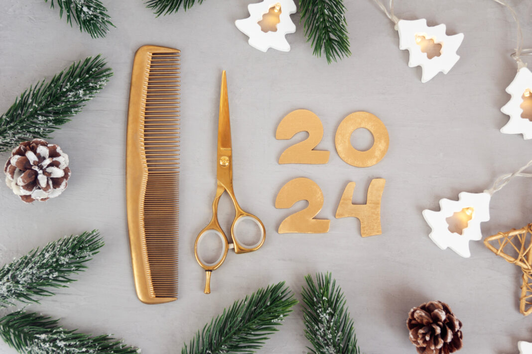 Numbers 2024 golden colored scissors and comb with fir twigs on gray background. Template greeting card of hairdresser or hair salon.