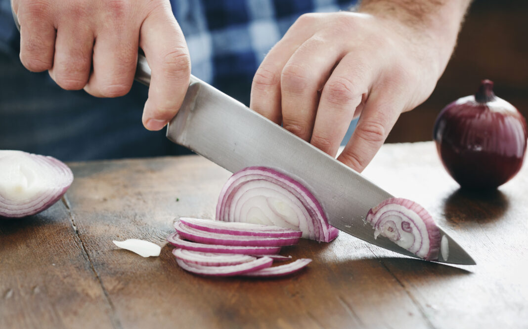 Male hands chopped red onion wooden table close up