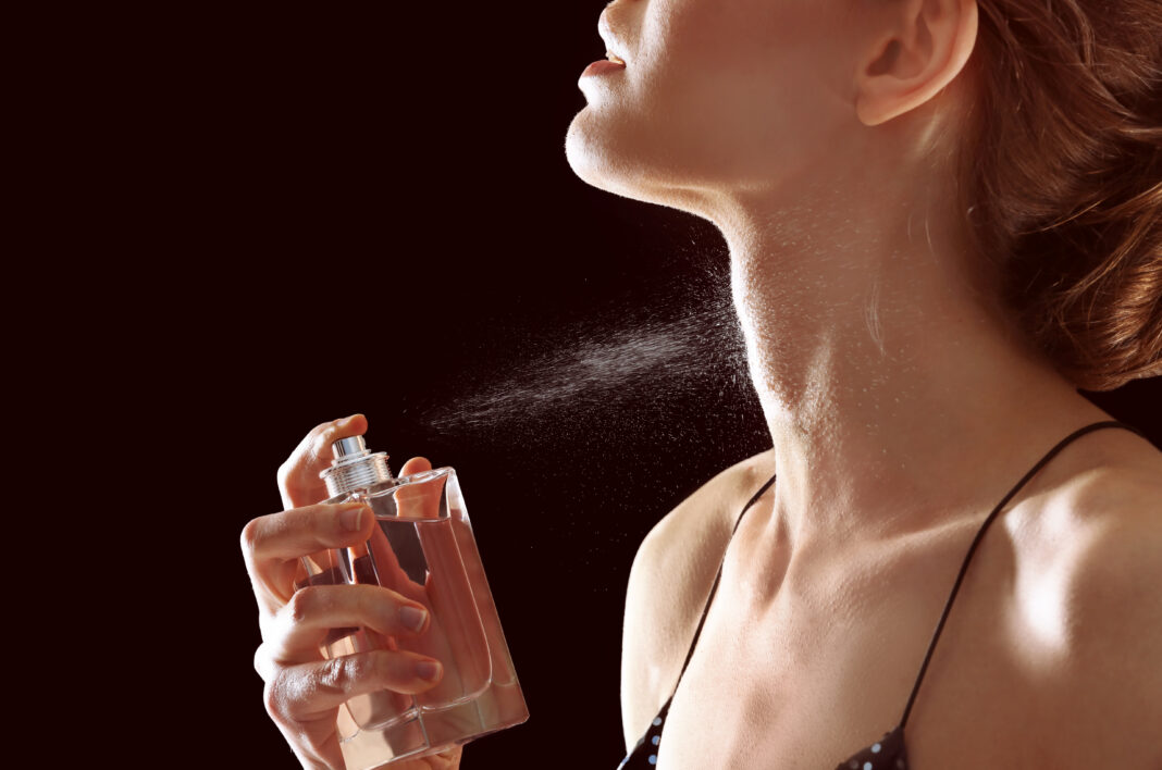 Beautiful young woman with bottle of perfume on dark background