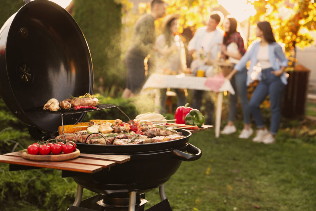 Group of friends having party outdoors. Focus on barbecue grill