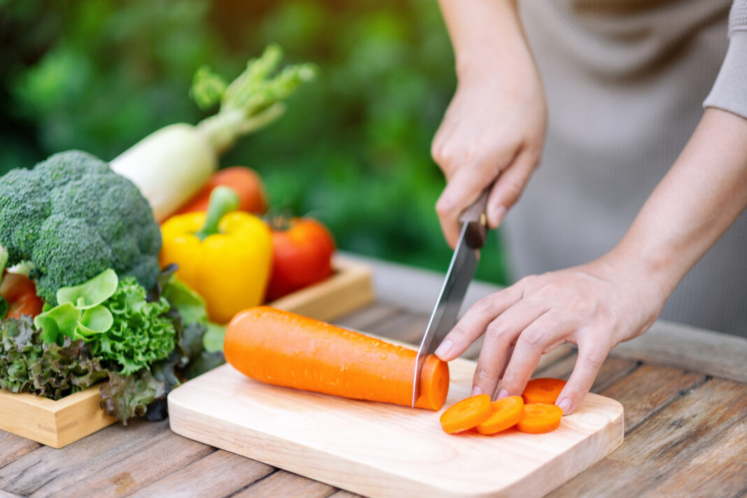 Closeup image of a woman cutting and chopping carrot by knife on wooden board