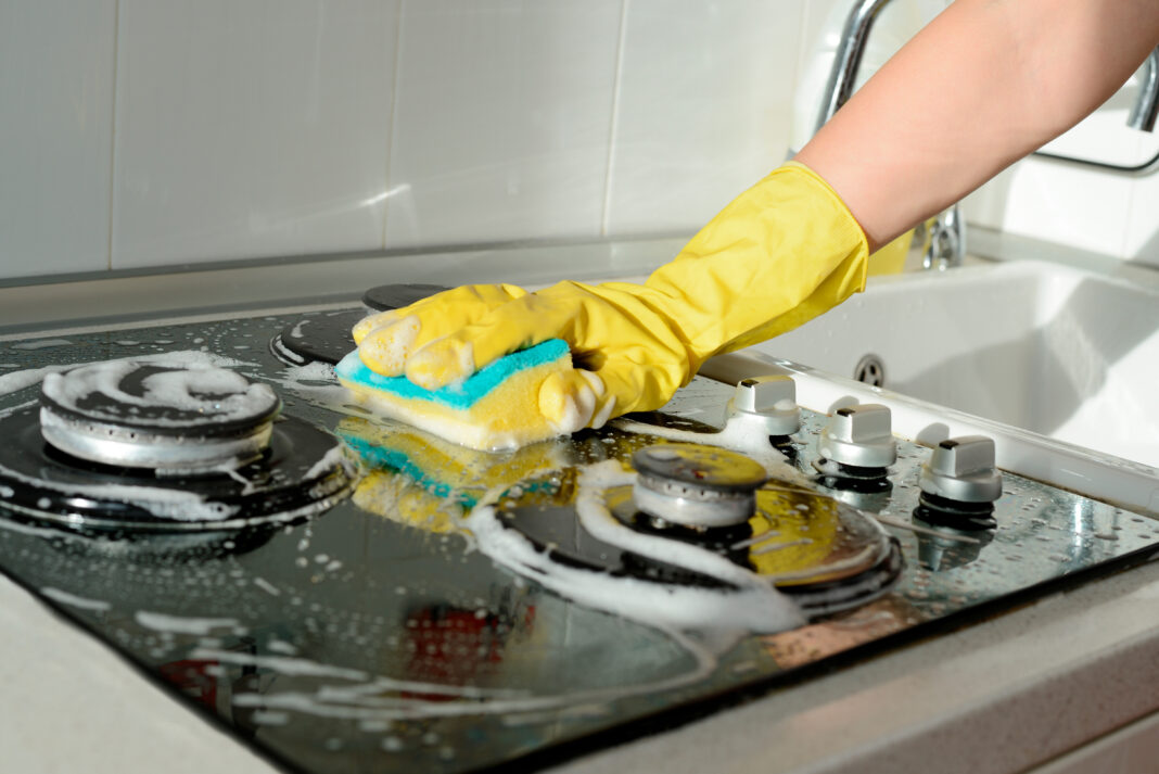 A hand in a yellow rubber glove washes a gas stove on a sunny da